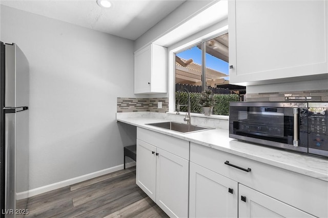 kitchen with appliances with stainless steel finishes, white cabinets, backsplash, a sink, and baseboards
