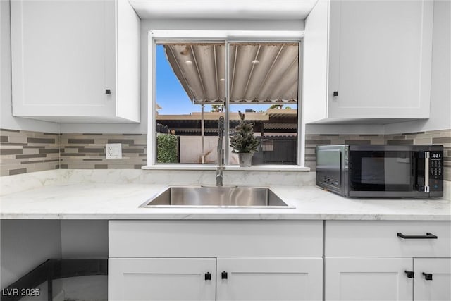 kitchen with black microwave, decorative backsplash, white cabinets, and a sink
