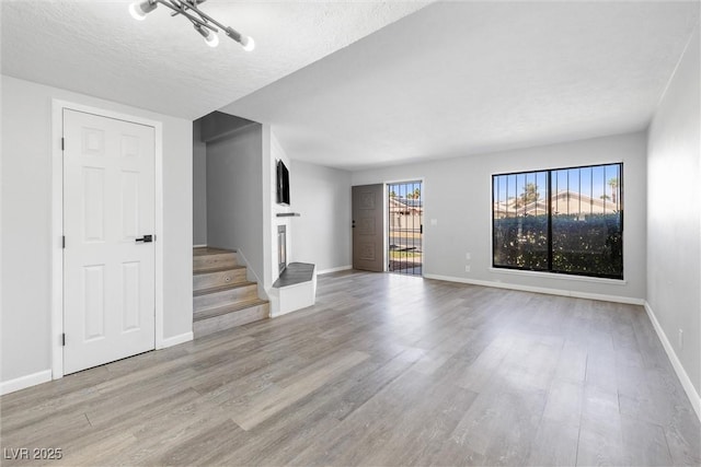 unfurnished living room with a textured ceiling, stairway, wood finished floors, and baseboards