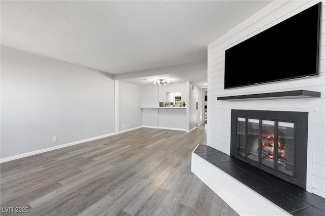 unfurnished living room with an inviting chandelier, a large fireplace, wood finished floors, and baseboards