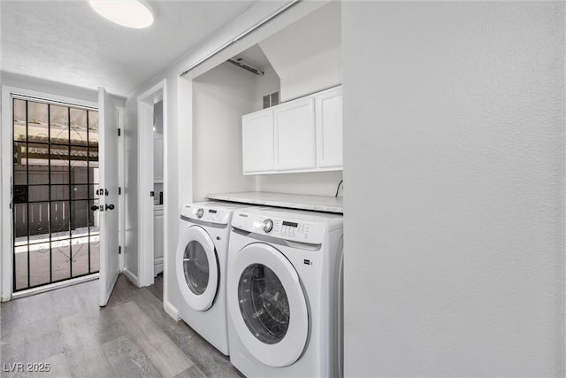 laundry room with washing machine and dryer, visible vents, cabinet space, and light wood-style floors