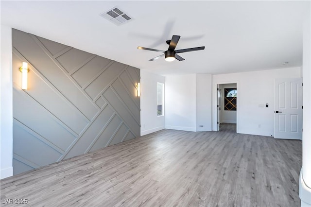 unfurnished room with visible vents, a decorative wall, baseboards, wood finished floors, and a ceiling fan