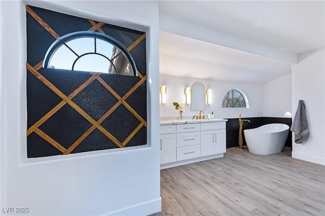 full bath with a sink, wood finished floors, double vanity, baseboards, and a soaking tub