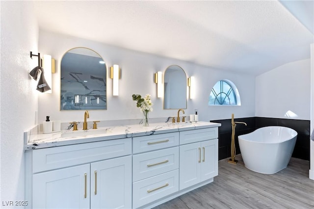 full bathroom featuring wood finished floors, a freestanding bath, double vanity, a sink, and lofted ceiling