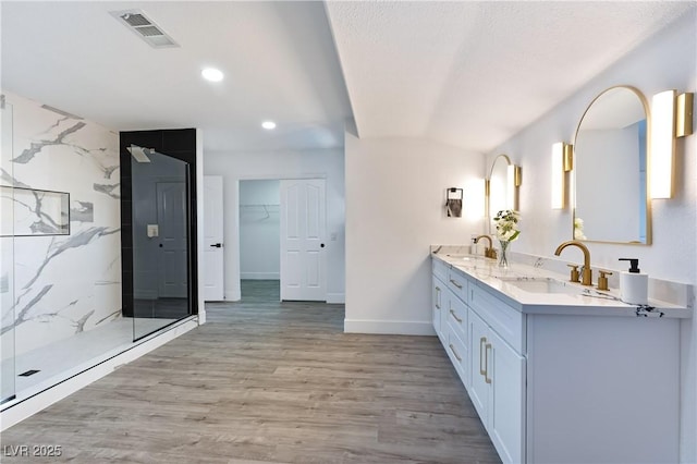bathroom featuring a marble finish shower, a sink, wood finished floors, and visible vents