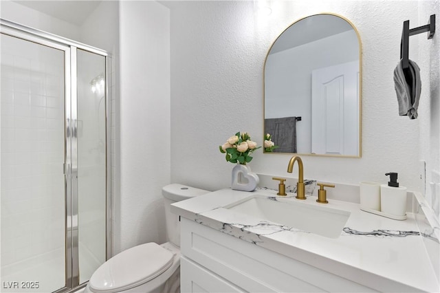 full bath featuring toilet, a stall shower, a textured wall, and vanity