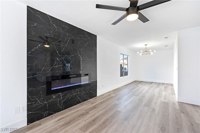 unfurnished living room featuring baseboards, an accent wall, wood finished floors, and ceiling fan with notable chandelier