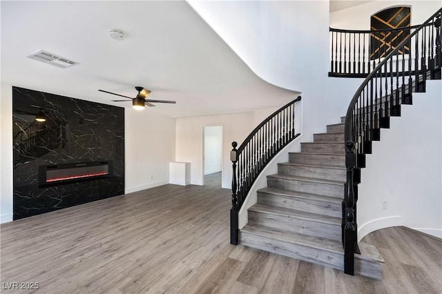 stairway with a fireplace, ceiling fan, visible vents, baseboards, and wood finished floors
