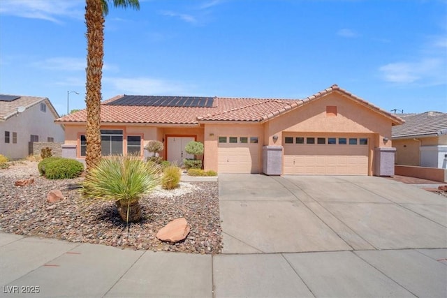 mediterranean / spanish-style house featuring a tiled roof, solar panels, concrete driveway, an attached garage, and stucco siding