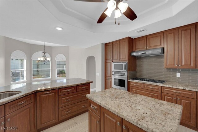 2595 Aviv Ct, Las Vegas, NV 89121 - kitchen featuring under cabinet range hood, brown cabinetry, appliances with stainless steel finishes, and a tray ceiling
