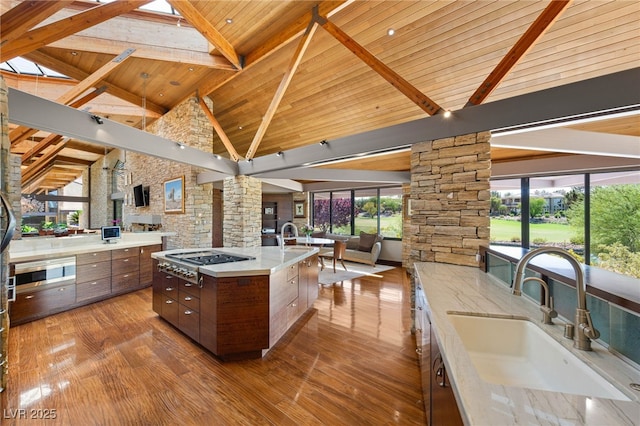 kitchen featuring high vaulted ceiling, decorative columns, stainless steel gas stovetop, and a sink
