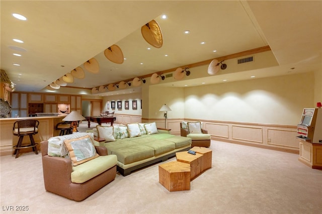 living area featuring visible vents, light carpet, wainscoting, and a decorative wall