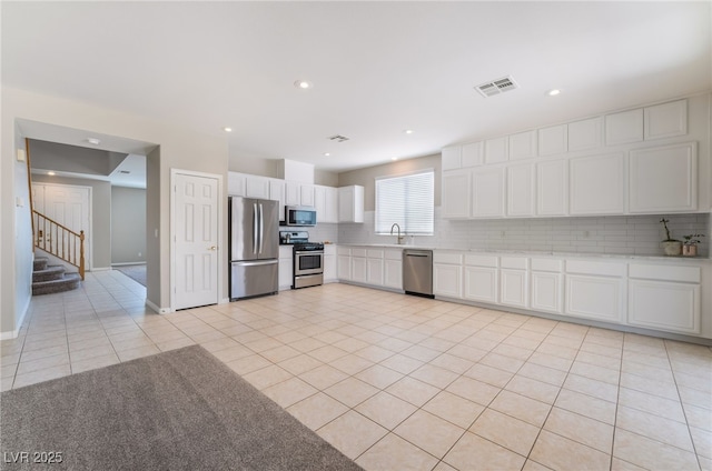 kitchen featuring decorative backsplash, stainless steel appliances, white cabinetry, and visible vents