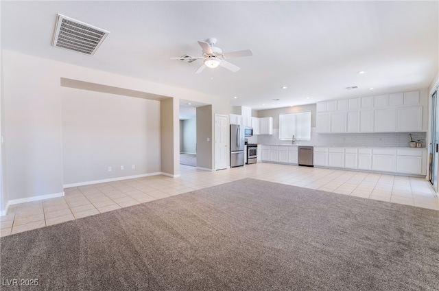 unfurnished living room featuring a ceiling fan, light colored carpet, visible vents, light tile patterned floors, and a sink