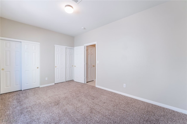 unfurnished bedroom with two closets, baseboards, and light colored carpet