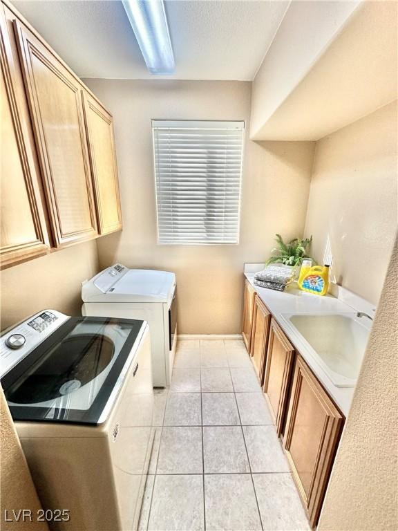 washroom with a sink, light tile patterned floors, cabinet space, and washer and clothes dryer