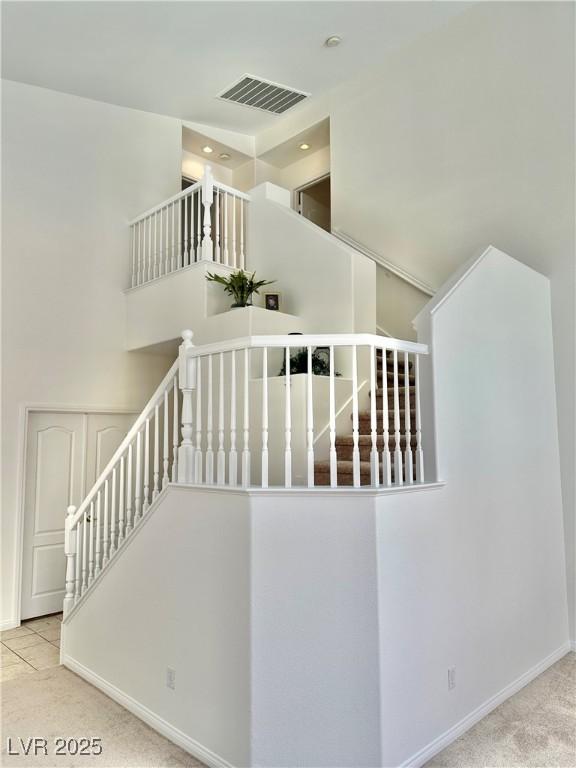 staircase featuring baseboards, visible vents, a high ceiling, and carpet