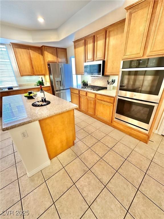 kitchen featuring a kitchen island, light tile patterned flooring, appliances with stainless steel finishes, and light stone counters