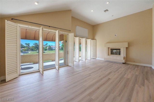 unfurnished living room featuring lofted ceiling, baseboards, wood finished floors, and a glass covered fireplace