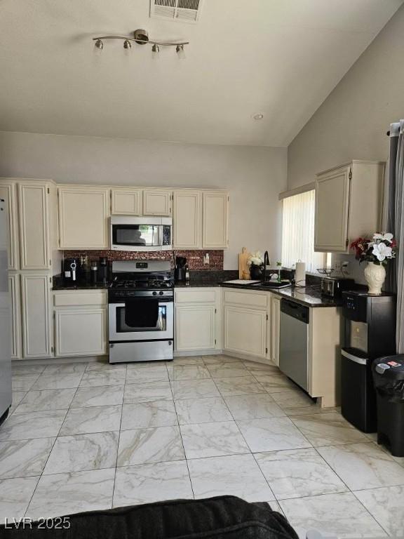 kitchen with a sink, stainless steel appliances, tasteful backsplash, marble finish floor, and dark countertops