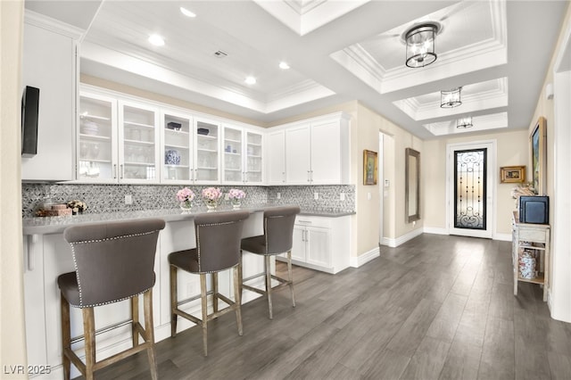 kitchen featuring a raised ceiling, a kitchen breakfast bar, white cabinets, and glass insert cabinets