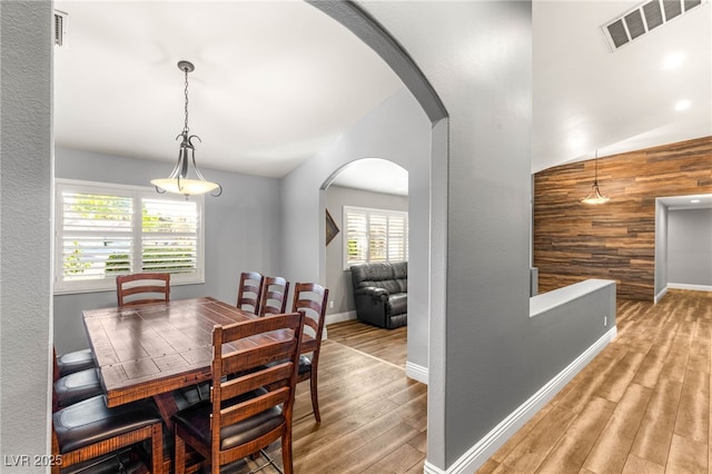 dining room with visible vents, baseboards, arched walkways, wooden walls, and wood finished floors