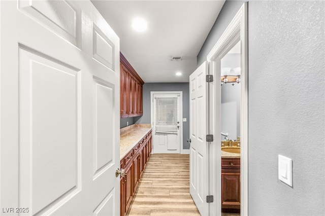corridor featuring visible vents, light wood-type flooring, and a sink