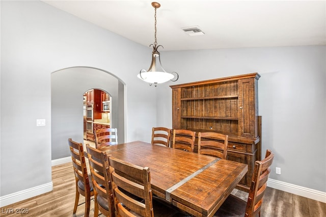 dining space with baseboards, visible vents, arched walkways, and light wood-type flooring