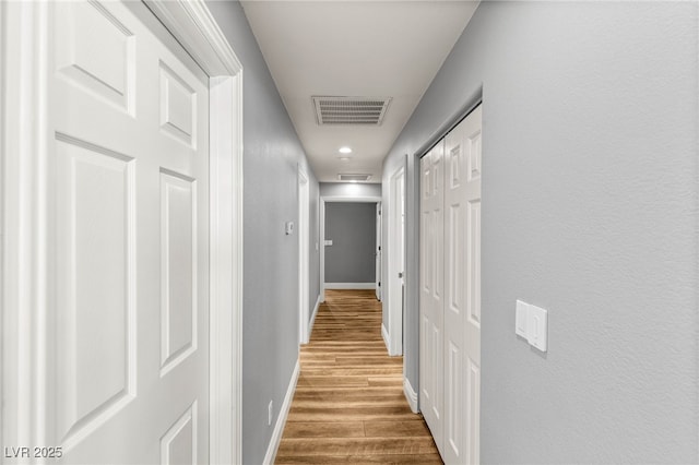 hallway featuring baseboards, visible vents, and wood finished floors