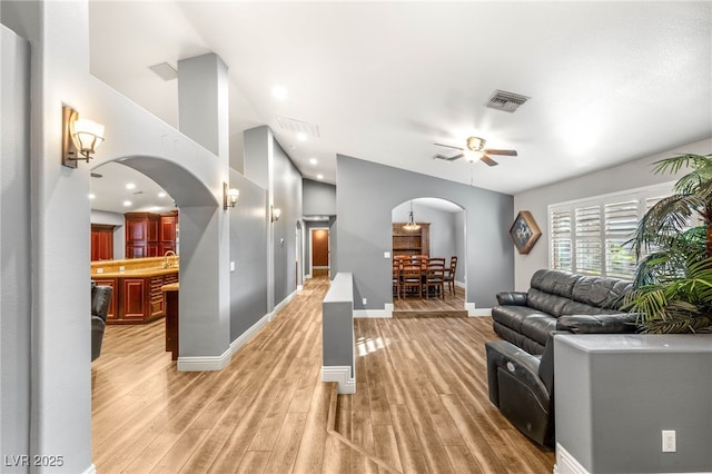 living area with ceiling fan, visible vents, light wood-style flooring, baseboards, and arched walkways