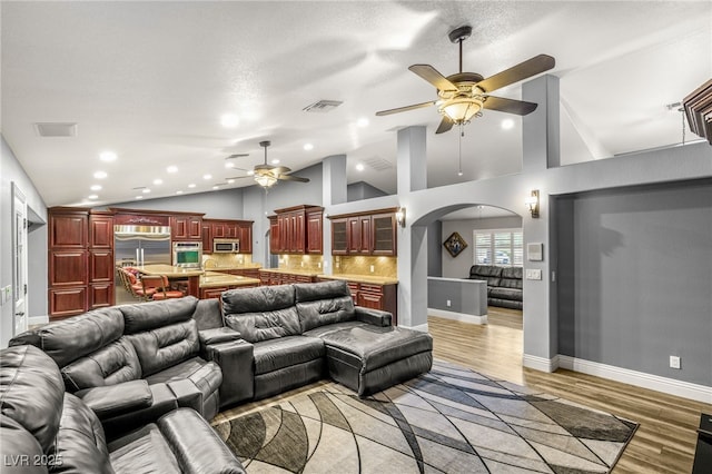 living room featuring visible vents, arched walkways, light wood-type flooring, a ceiling fan, and lofted ceiling