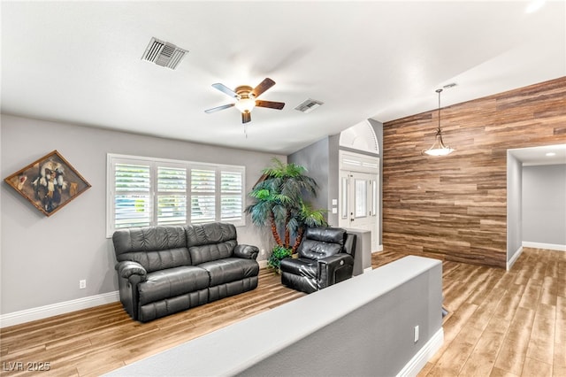 living room featuring wooden walls, visible vents, ceiling fan, and wood finished floors