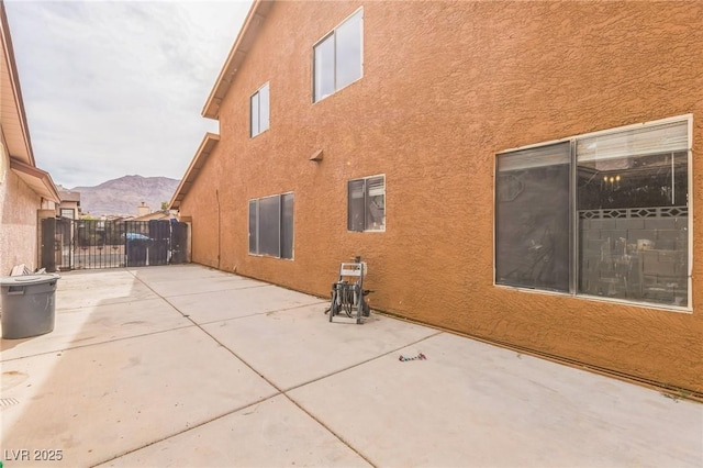rear view of property featuring stucco siding, a gate, fence, a patio area, and a mountain view