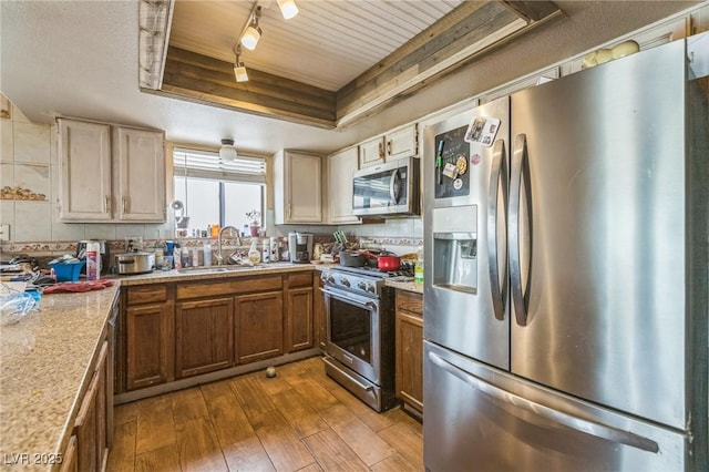 kitchen with a sink, stainless steel appliances, a raised ceiling, dark wood-type flooring, and light countertops