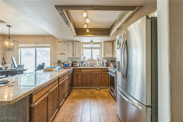 kitchen featuring brown cabinetry, stainless steel appliances, light wood-type flooring, a peninsula, and a tray ceiling