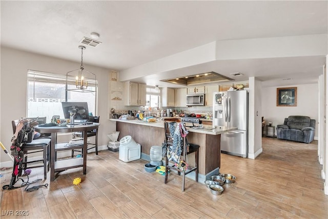 kitchen featuring stainless steel appliances, light countertops, light wood-type flooring, visible vents, and a peninsula
