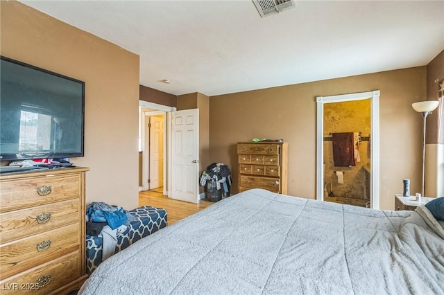 bedroom with visible vents, wood finished floors, and ensuite bath