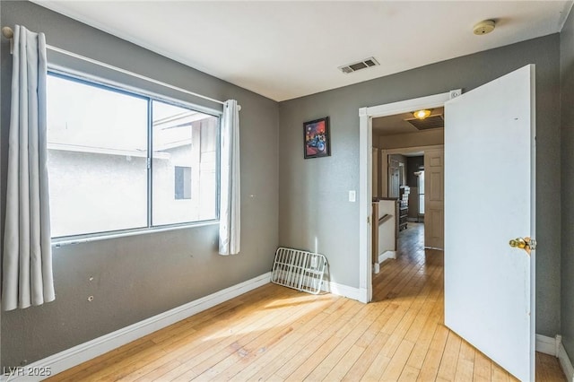 empty room with visible vents, light wood-type flooring, and baseboards