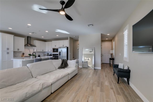 living area featuring visible vents, ceiling fan, light wood finished floors, and baseboards