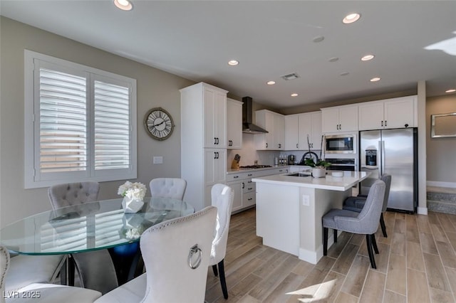 kitchen with stainless steel appliances, a kitchen breakfast bar, wall chimney exhaust hood, visible vents, and white cabinetry