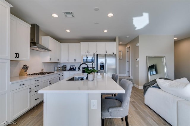 kitchen featuring stainless steel appliances, a kitchen bar, a sink, visible vents, and wall chimney exhaust hood