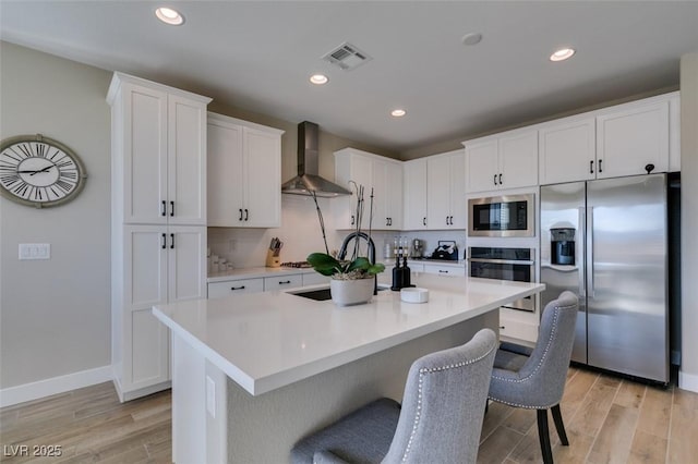 kitchen with visible vents, stainless steel appliances, light wood-style floors, and wall chimney exhaust hood