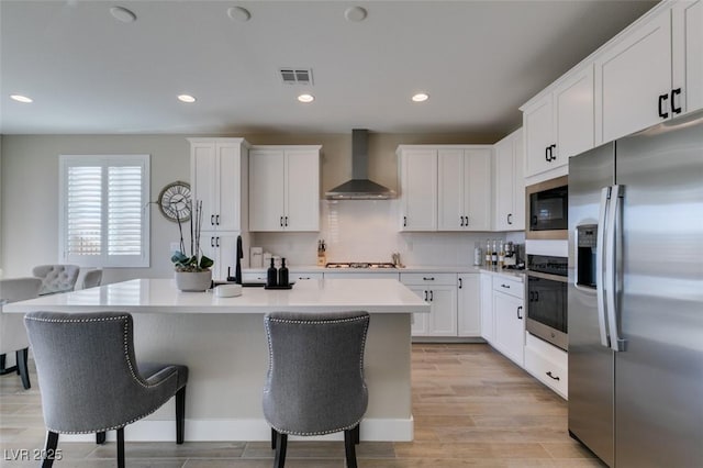 kitchen with appliances with stainless steel finishes, a kitchen island, white cabinets, a kitchen bar, and wall chimney exhaust hood