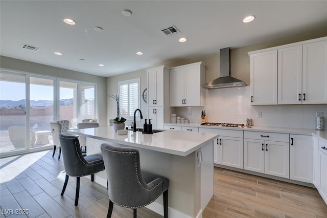 kitchen featuring visible vents, wall chimney exhaust hood, a kitchen breakfast bar, and a sink