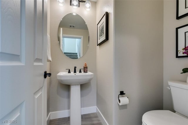 bathroom featuring toilet, a sink, wood finished floors, and baseboards