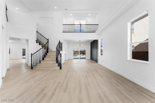 entrance foyer with a high ceiling, a chandelier, light wood-style flooring, stairs, and baseboards