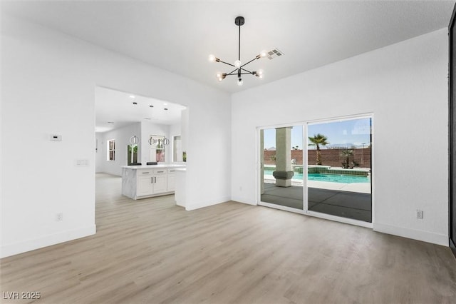 unfurnished living room with light wood-style floors, baseboards, a notable chandelier, and visible vents