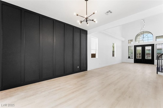 unfurnished living room with a towering ceiling, light wood finished floors, a chandelier, and visible vents