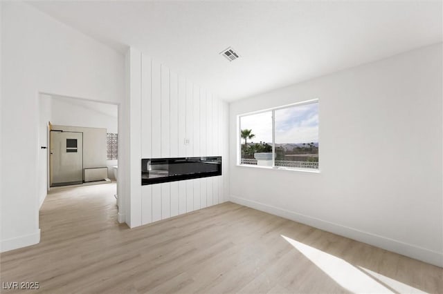 unfurnished living room with baseboards, light wood finished floors, a large fireplace, and visible vents