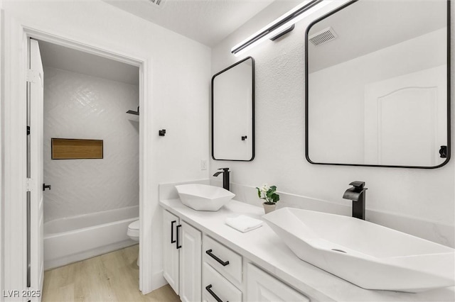 bathroom featuring double vanity, toilet, a sink, and wood finished floors